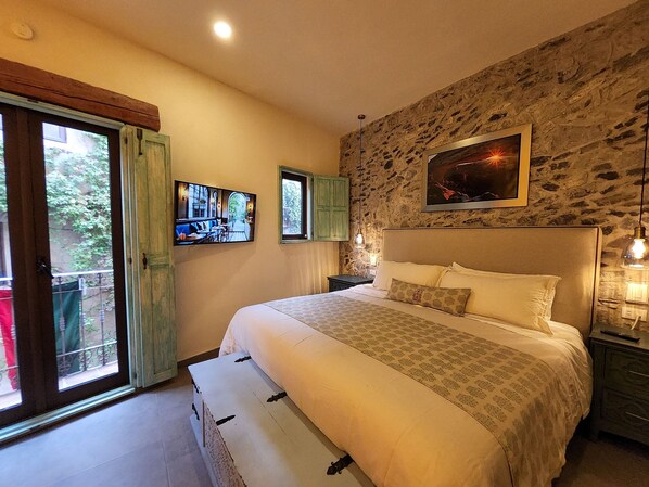 A bedroom with a large bed, a stone wall, a painting, and a window with a view.