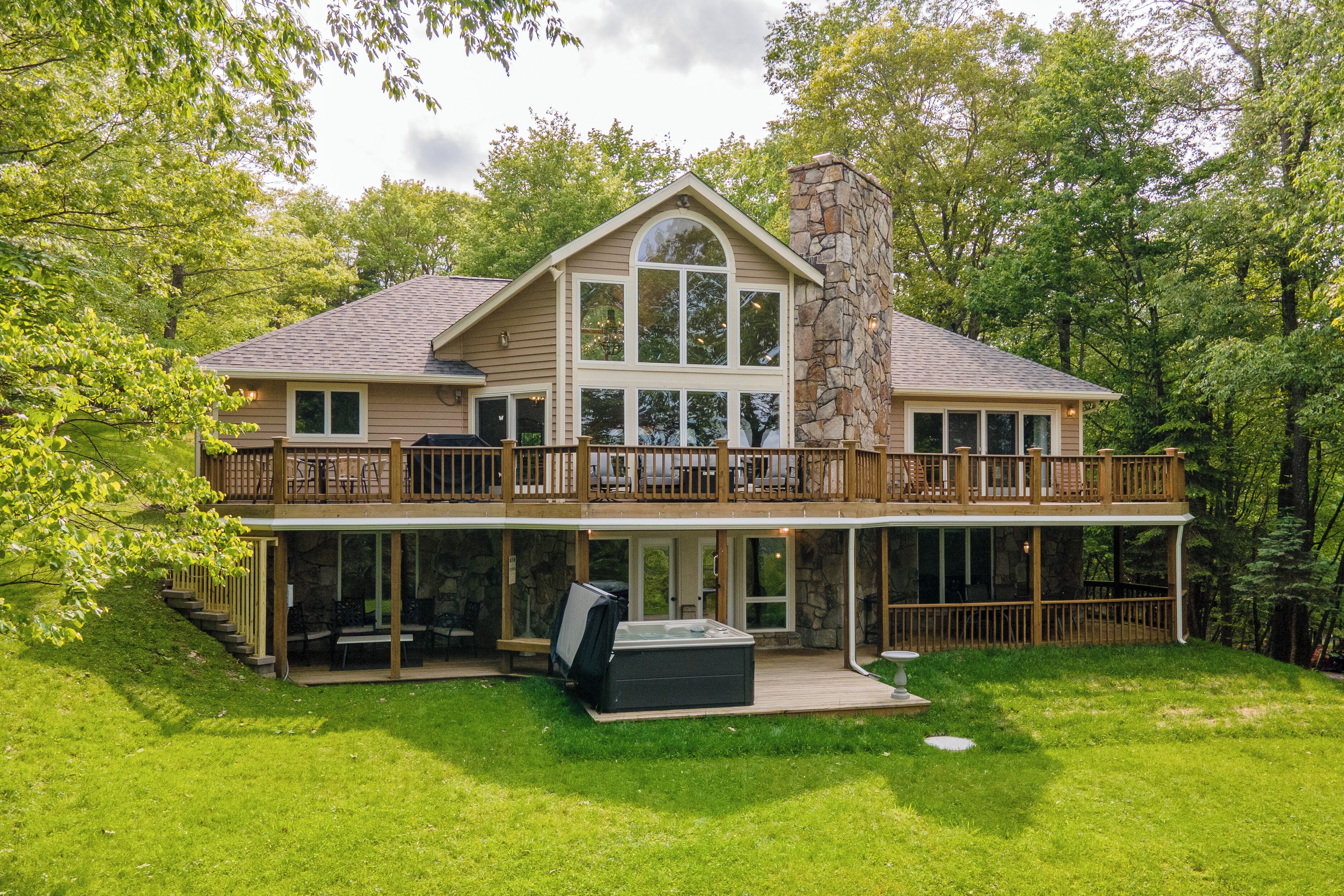 A two-story house with a stone fireplace, a covered patio, and a hot tub.