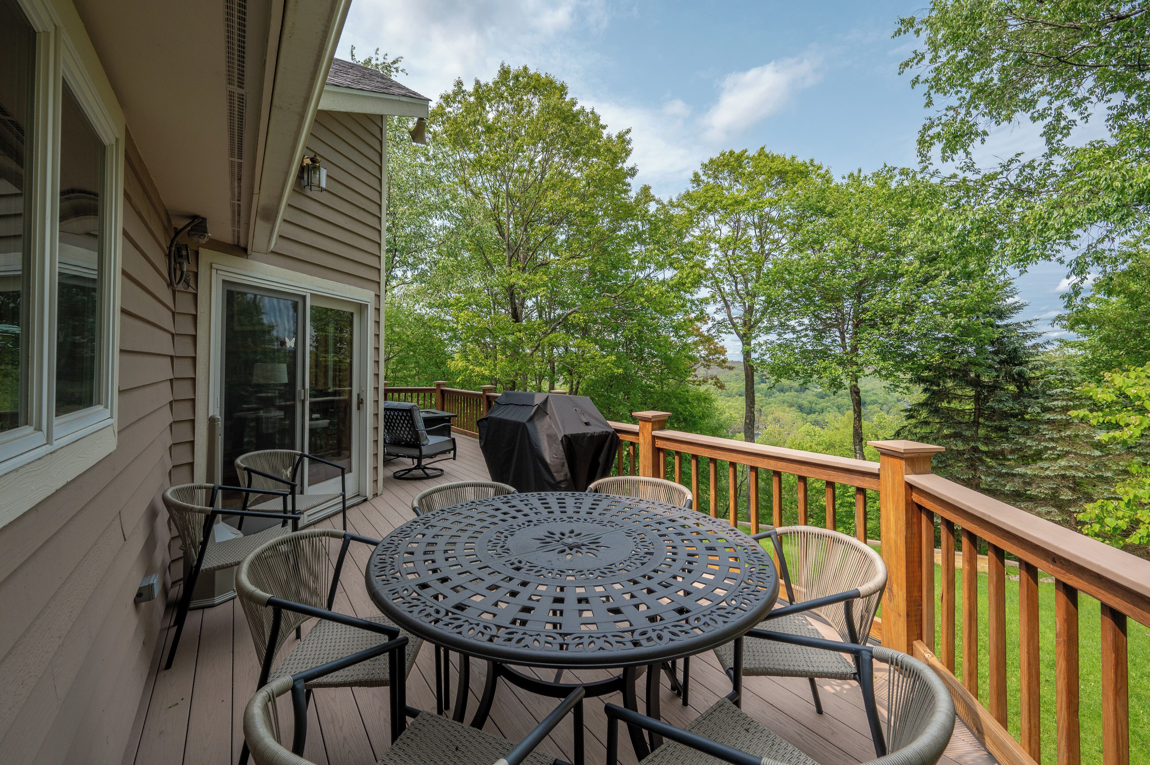 Un terrazzo con tavolo e sedie rotonde, un barbecue e vista su alberi e colline.