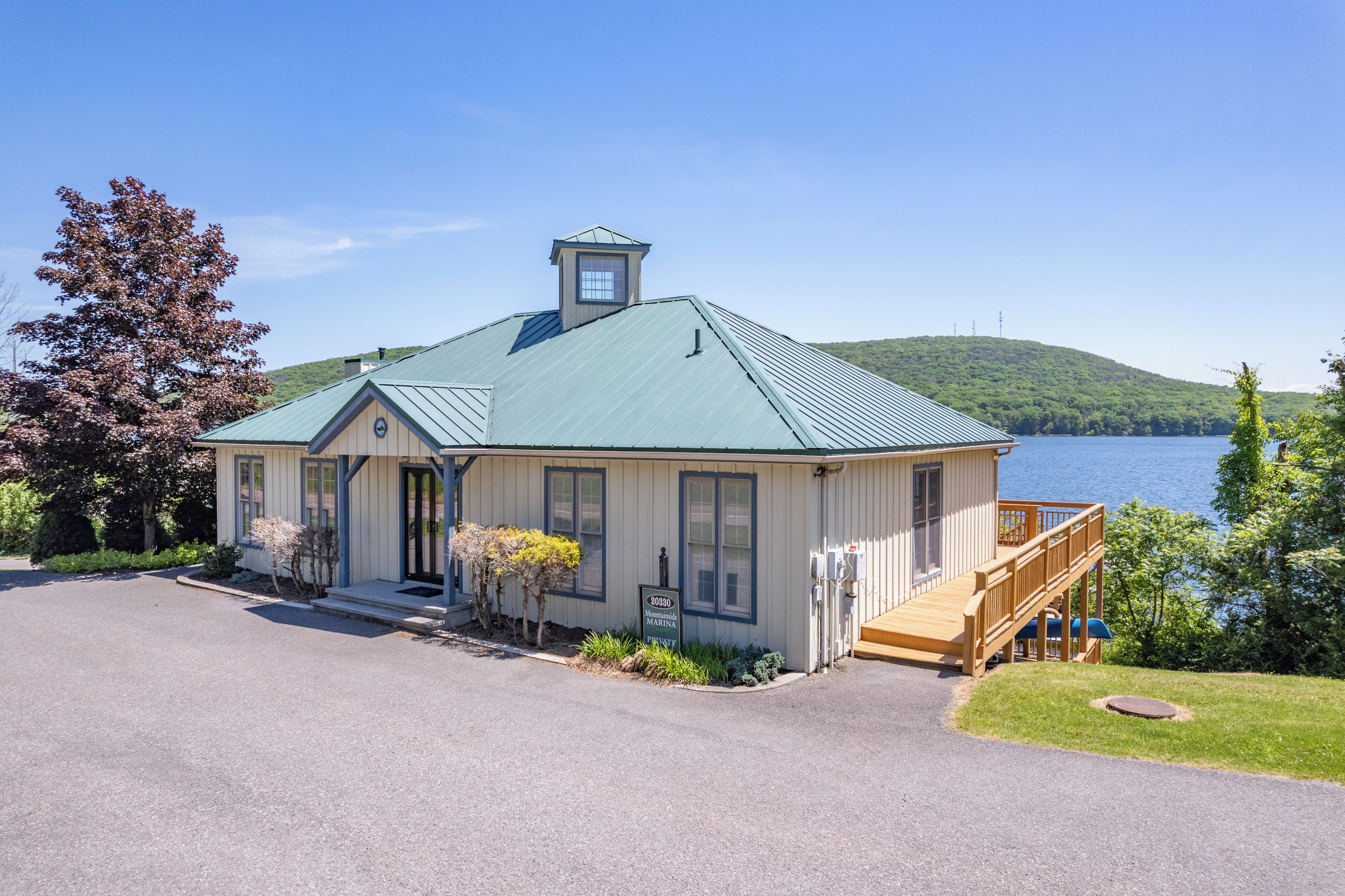 A single-story house with a green roof, a front porch, and a deck overlooking a lake.