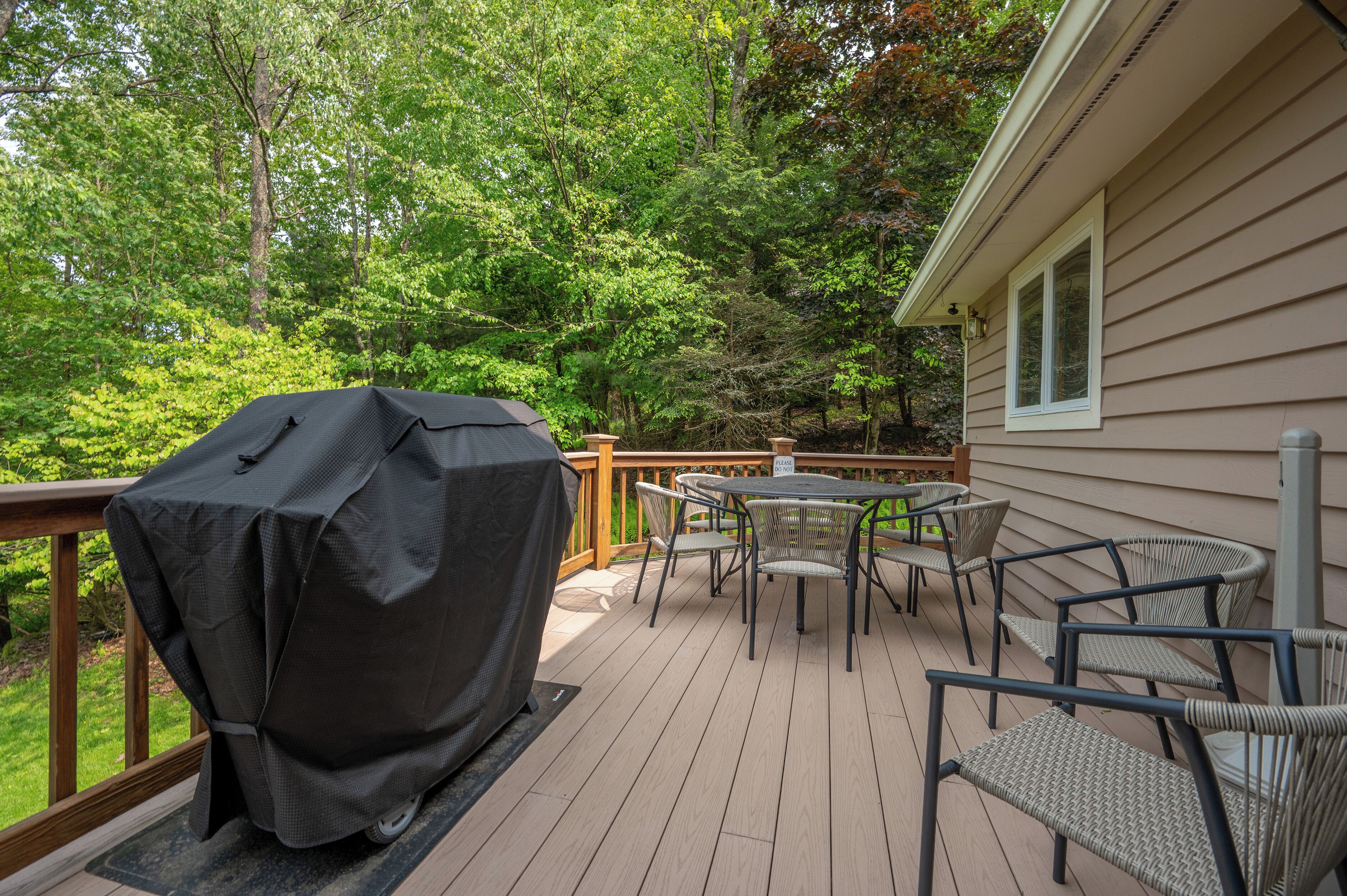 A deck with a grill, outdoor table, and chairs, surrounded by trees.