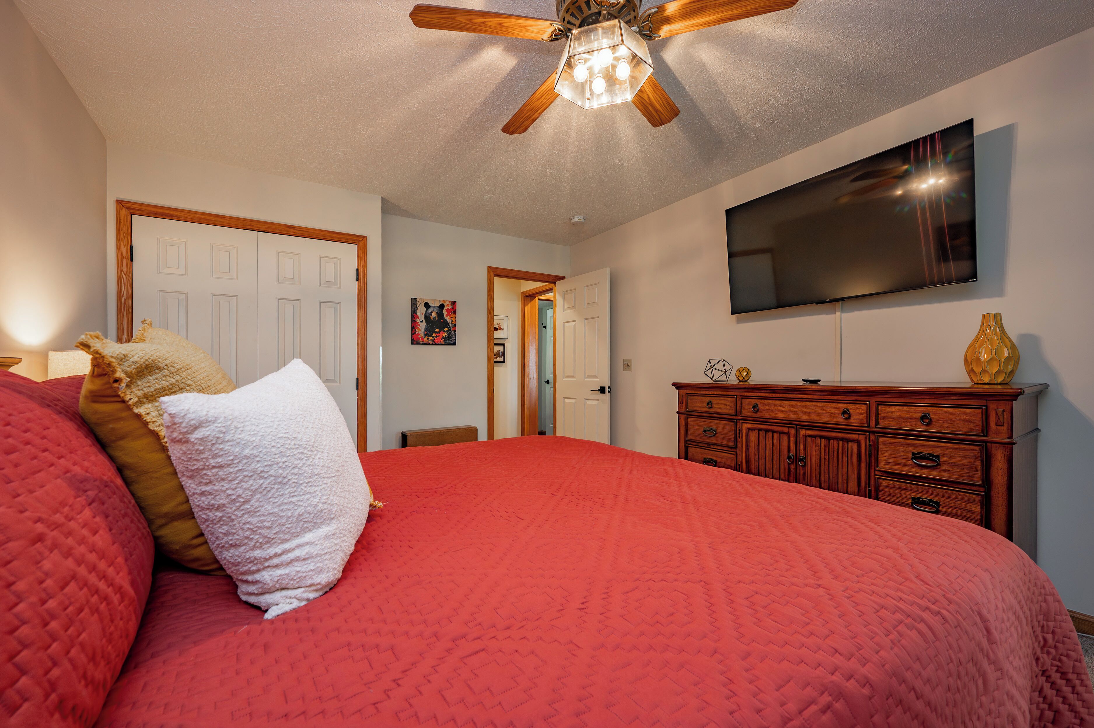 A bedroom with a large bed, a ceiling fan, a flat-screen TV, and a wooden dresser.