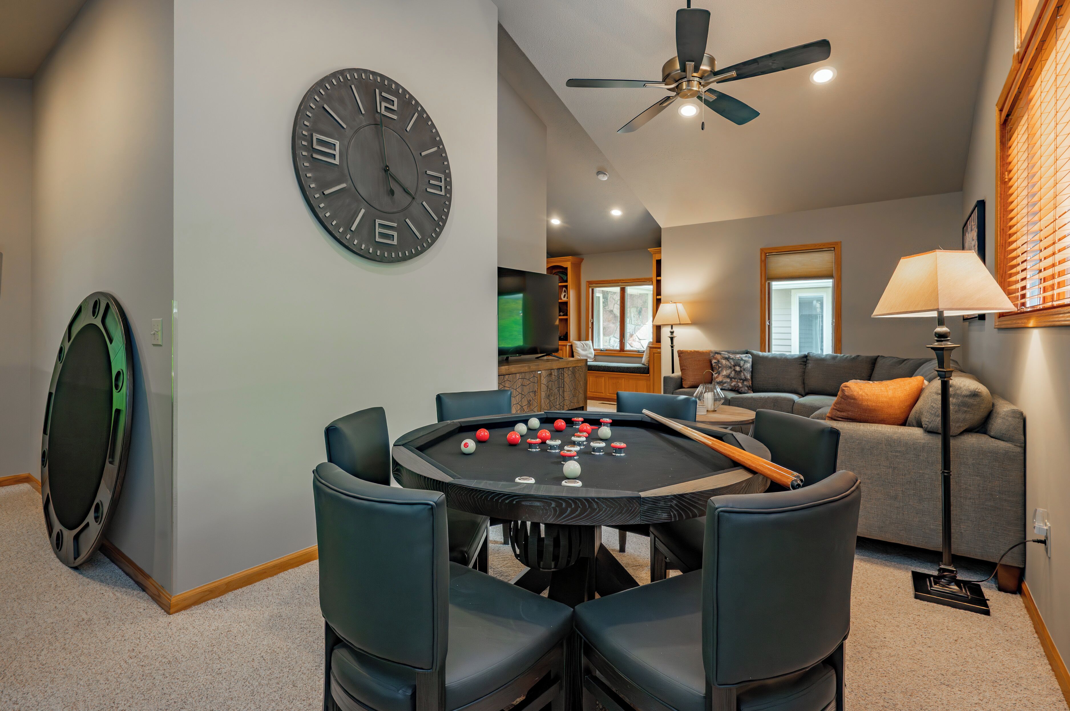 A pool table with chairs, a clock, a ceiling fan, and a sofa in a living room.