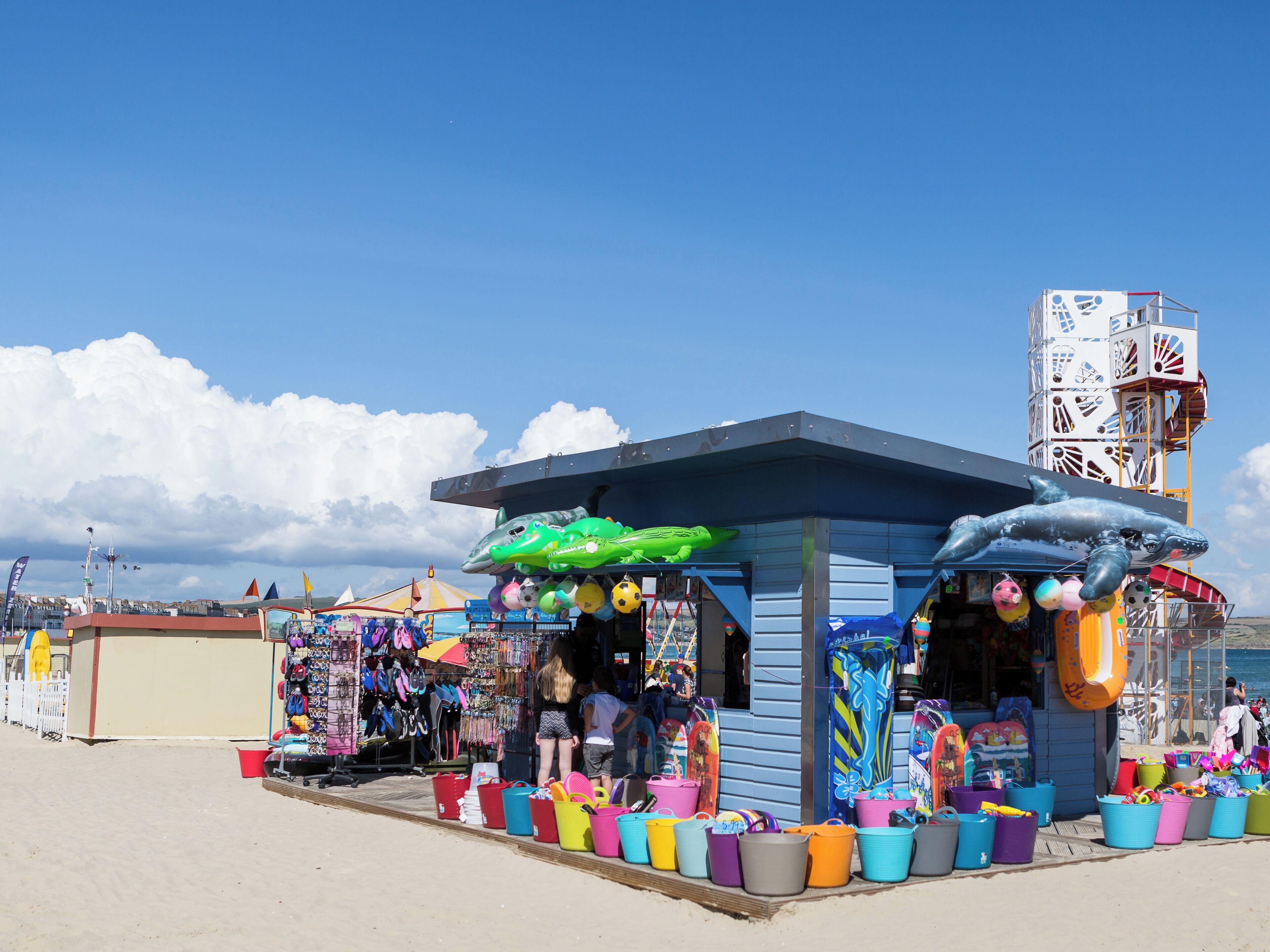 Un petit kiosque situé au bord de la plage, où l’on vend des jouets et des accessoires colorés pour la plage.