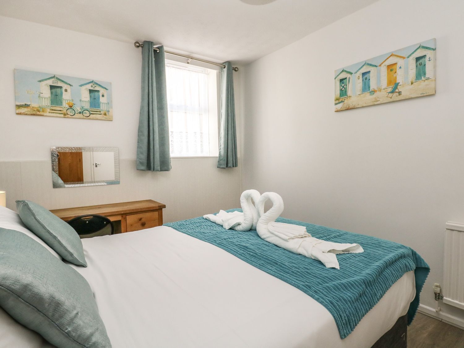 A bedroom with a bed, a wooden nightstand, a mirror, and two paintings of beach houses.