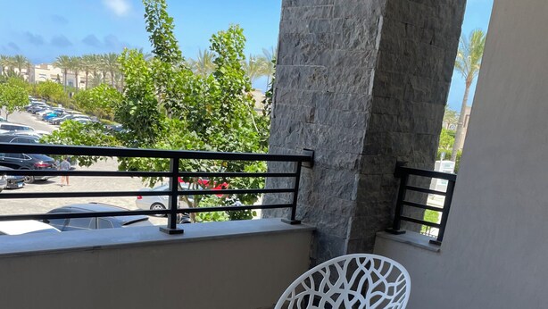 A balcony with a white table and chairs, a stone pillar, and a view of parked cars and palm trees.