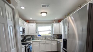 A kitchen with white cabinets, stainless steel appliances, and a window providing natural light. - 4 min walk Ocean View Sleeps 14.  Pet Ramp. Fenced Yard. King Bed 75" TV (Bolivar Peninsula)