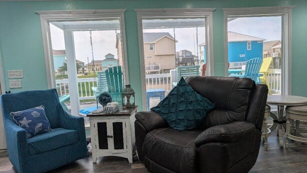 A living room with a blue armchair, a brown leather sofa, and a small table with a lamp. - 4 min walk Ocean View Sleeps 14.  Pet Ramp. Fenced Yard. King Bed 75" TV (Bolivar Peninsula)
