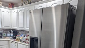 A stainless steel refrigerator in a kitchen with white cabinets and a herringbone-patterned floor. - 4 min walk Ocean View Sleeps 14.  Pet Ramp. Fenced Yard. King Bed 75" TV (Bolivar Peninsula)
