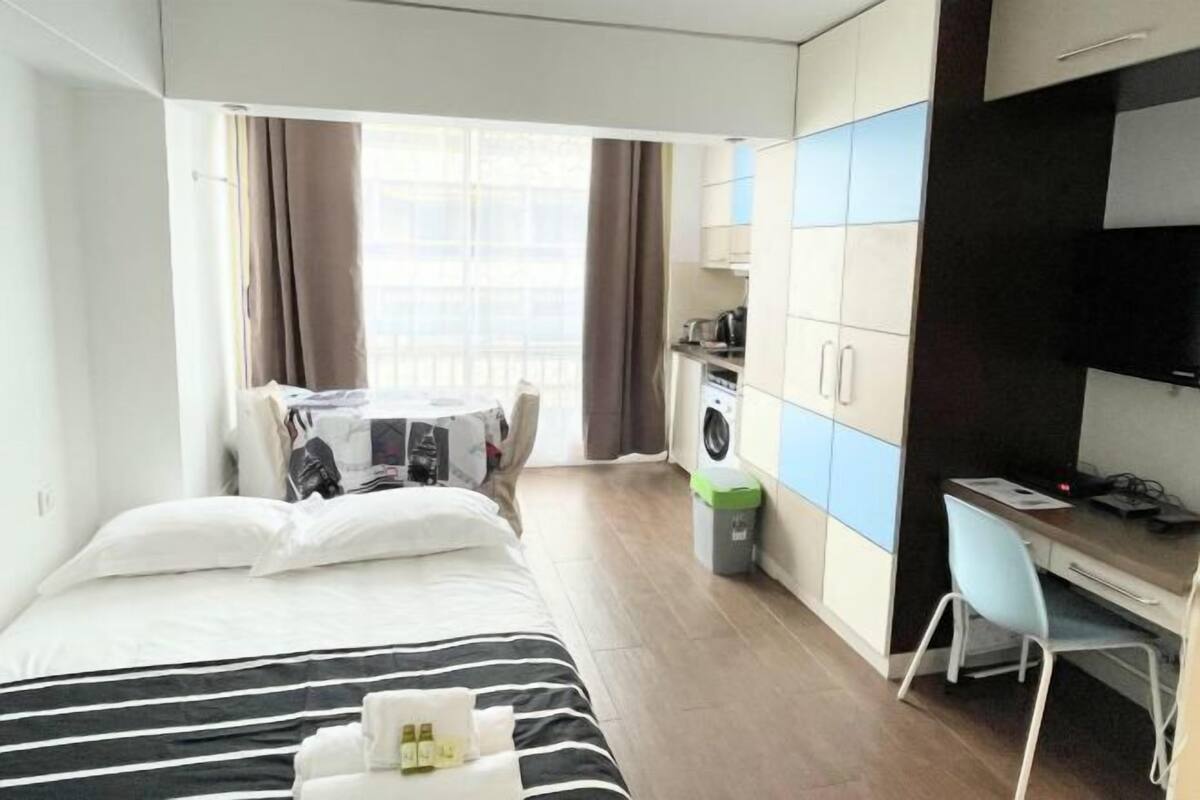 A hotel room with a bed, a desk, a washing machine, and a TV.