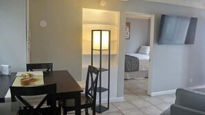 Un espace de vie compact comprenant un coin repas, un lit et un téléviseur fixé au mur.