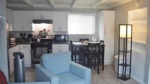 Une cuisine compacte avec des meubles blancs, un coin repas comprenant une table et des chaises, et un canapé bleu.