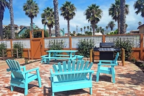Relax in style with four Adirondack chairs surrounding a central table, set amidst a tranquil patio with a barbecue grill nearby.