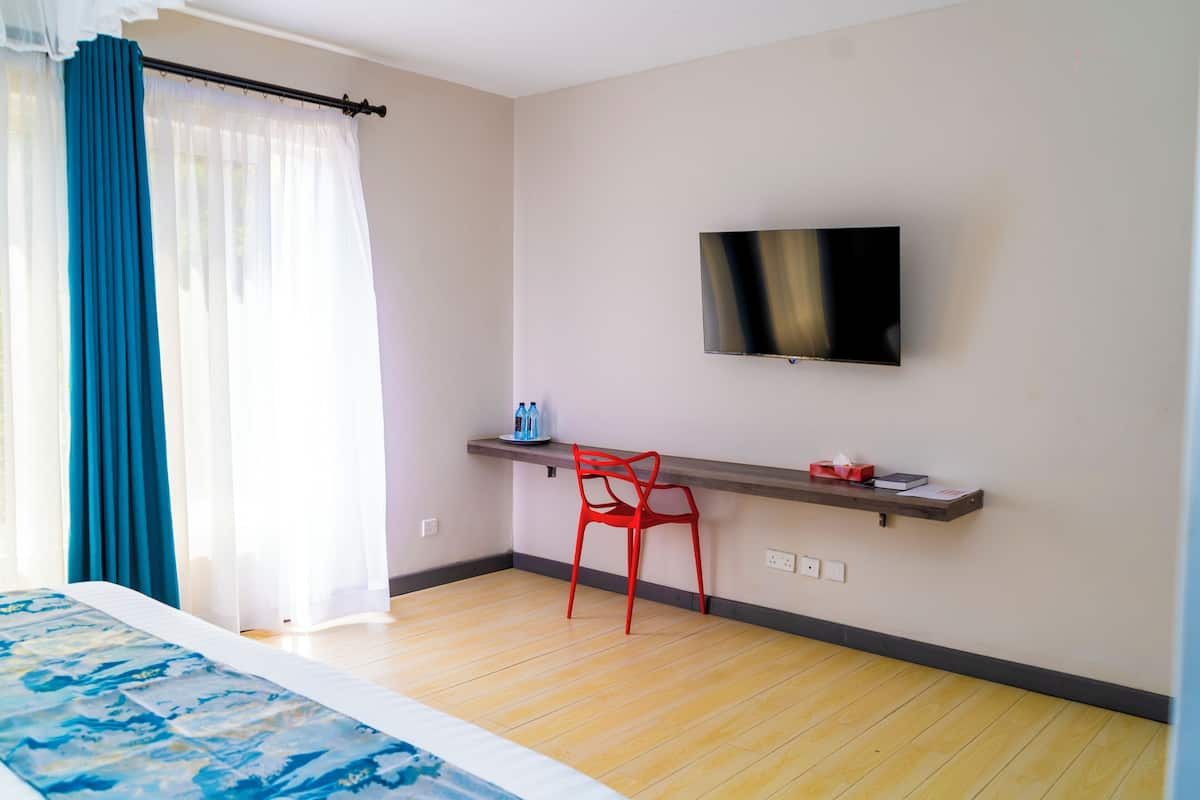 Habitación de hotel con cama, televisor montado en la pared, una silla roja y un estante con artículos de aseo.