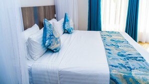 Una cama bien hecha con sábanas blancas y almohadas con estampado azul, un cabecero de madera y una colcha con estampado azul.