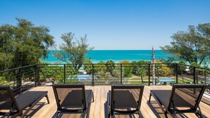 Eine Holzterrasse mit Liegestühlen mit Blick auf ein klares, blaues Meer und einen angelegten Garten.