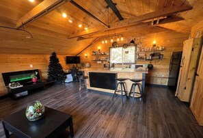 A cozy cabin interior with a wooden ceiling, a kitchen area with a bar, and a Christmas tree. - Charming "Melrose Place" w Year-Round Heated Pool, Deck & Grill (Victoria)