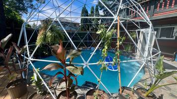 A geodesic greenhouse structure with a pool and potted plants.
