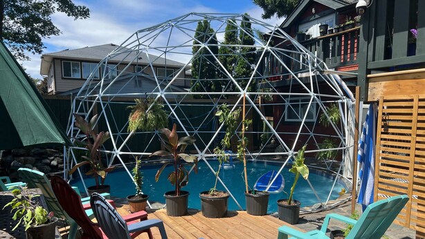 A geodesic dome structure over a swimming pool with potted plants and outdoor furniture. - Charming "Melrose Place" w Year-Round Heated Pool, Deck & Grill (Victoria)