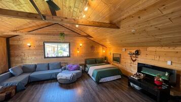 A cozy room with a wooden ceiling, a sofa, a bed, a TV, and a window.