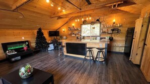 A cozy cabin interior with a wooden ceiling, a kitchen area with a bar, and a Christmas tree. - Charming "Melrose Place" w Year-Round Heated Pool, Deck & Grill (Victoria)
