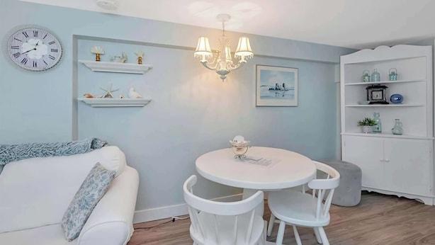 A dining area with a round table, white chairs, a chandelier, and a white cabinet with shelves. - Quaint 1 Bedroom Suite, Victoria, BC (Victoria)