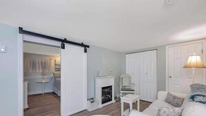 A modern living room with a white sofa, a fireplace, a sliding door leading to a bedroom, and a lamp on a side table. - Quaint 1 Bedroom Suite, Victoria, BC (Victoria)