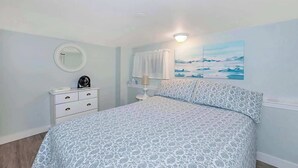 A bedroom with a bed, a bedside table, a lamp, a mirror, and a painting on the wall. - Quaint 1 Bedroom Suite, Victoria, BC (Victoria)