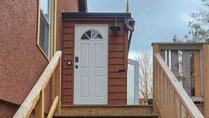 A wooden staircase leading to a white door with a small window above it, set against a red building facade. - Quaint Attic Suite w/ Heated Pool (Year-Round) (Victoria)