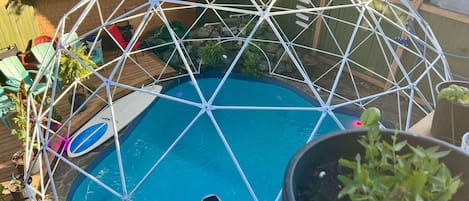 Eine geodätische Kuppel über einem Schwimmbecken mit Blumentöpfen und Gartenmöbeln.