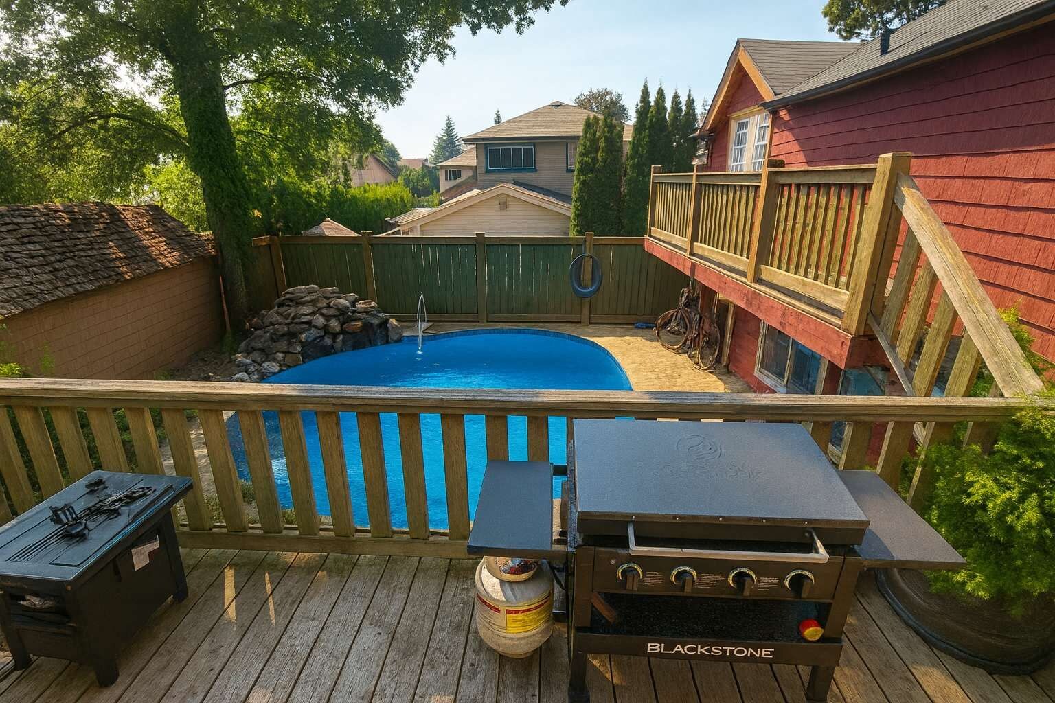 Un jardin avec une piscine, un barbecue et une terrasse en bois.