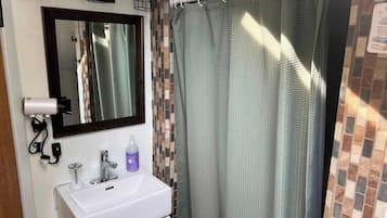 A bathroom with a white sink, a mirror, a shower curtain, and a tiled wall.