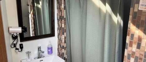 Une salle de bain avec un lavabo blanc, un miroir, un rideau de douche et un mur carrelé.
