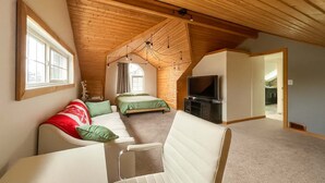 A loft bedroom with a sloped ceiling, a bed, a TV, and a seating area with a couch and chairs. - Quaint Attic Suite w/ Heated Pool (Year-Round) (Victoria)