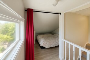 A bedroom with a bed, a window, a red curtain, and a staircase.