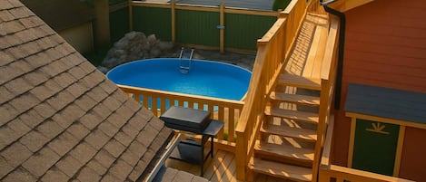 Ein Garten mit Schwimmbad, Holzterrasse und einem kleinen Tisch mit Stühlen.