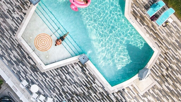 Vue aérienne d’une piscine agrémentée d’un flotteur en forme de flamant rose, entourée de chaises longues et de palmiers.
