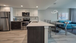 Une cuisine moderne dotée d’un îlot central, d’appareils électroménagers en acier inoxydable et d’un coin repas avec un canapé bleu et un luminaire suspendu.
