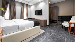 A modern hotel room with a large bed, a desk, a TV mounted on the wall, and a seating area with a chair and table. - The Azaria Hotel and Apartments (Lekki)