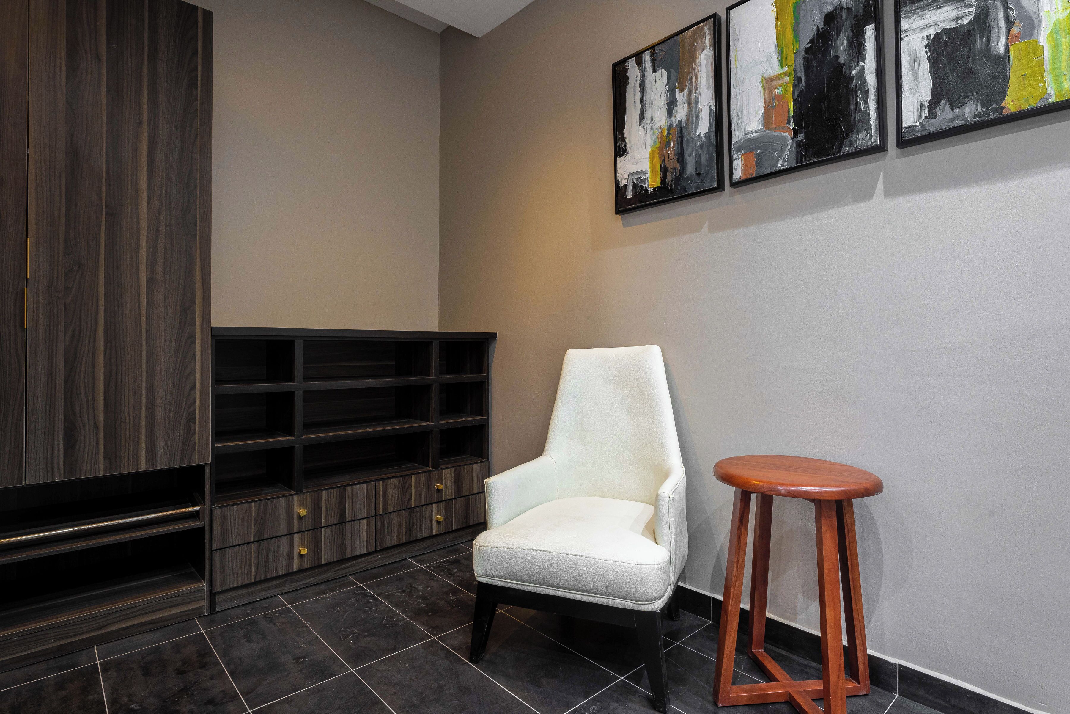 Ein modernes Interieur mit einem weißen Sessel, einem Holzschemel und einer schwarzen Unterhaltungsanlage an einer beigen Wand.