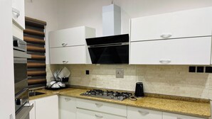 A modern kitchen with white cabinets, a gas stove, a black range hood, and a granite countertop. - The Azaria Hotel and Apartments (Lekki)