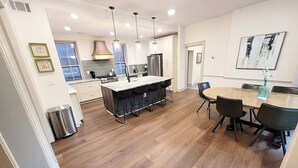 A modern kitchen with a central island, pendant lighting, and a dining area with a round table and chairs.