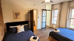 A hotel room with two beds, a ceiling fan, a door leading to a balcony, and a framed artwork on the wall.