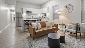 A modern living room with a brown leather sofa, two black side tables, a coffee table, and a dining area with a kitchen in the background. - Washington Park Retreat | Free Parking | OTR (Cincinnati)