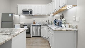 A modern kitchen with white cabinetry, stainless steel appliances, and a marble countertop. - Washington Park Retreat | Free Parking | OTR (Cincinnati)