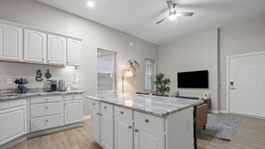 A modern kitchen with white cabinetry, a marble countertop island, and a ceiling fan. - Washington Park Retreat | Free Parking | OTR (Cincinnati)