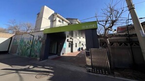A hotel entrance with a green sign, a mural on the wall, and a gated driveway.