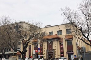 Een gebouw met een traditionele architectuur, met een opvallende ingang met een rode luifel en een bord boven de deur. Voor het gebouw staan bomen, en er zijn verschillende auto's langs de straat geparkeerd.