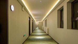 A long, narrow hotel corridor with a carpeted floor, illuminated by overhead lights, and doors on both sides.