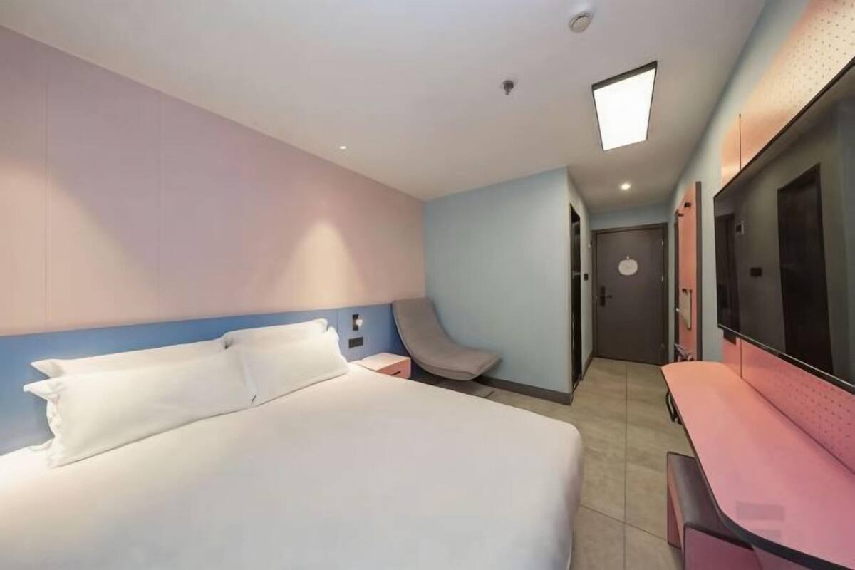 A hotel room with a bed, bedside table, chair, desk, and a TV.